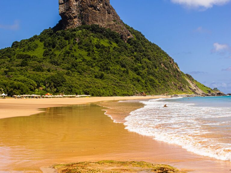 Praia com grande formação rochosa ao fundo